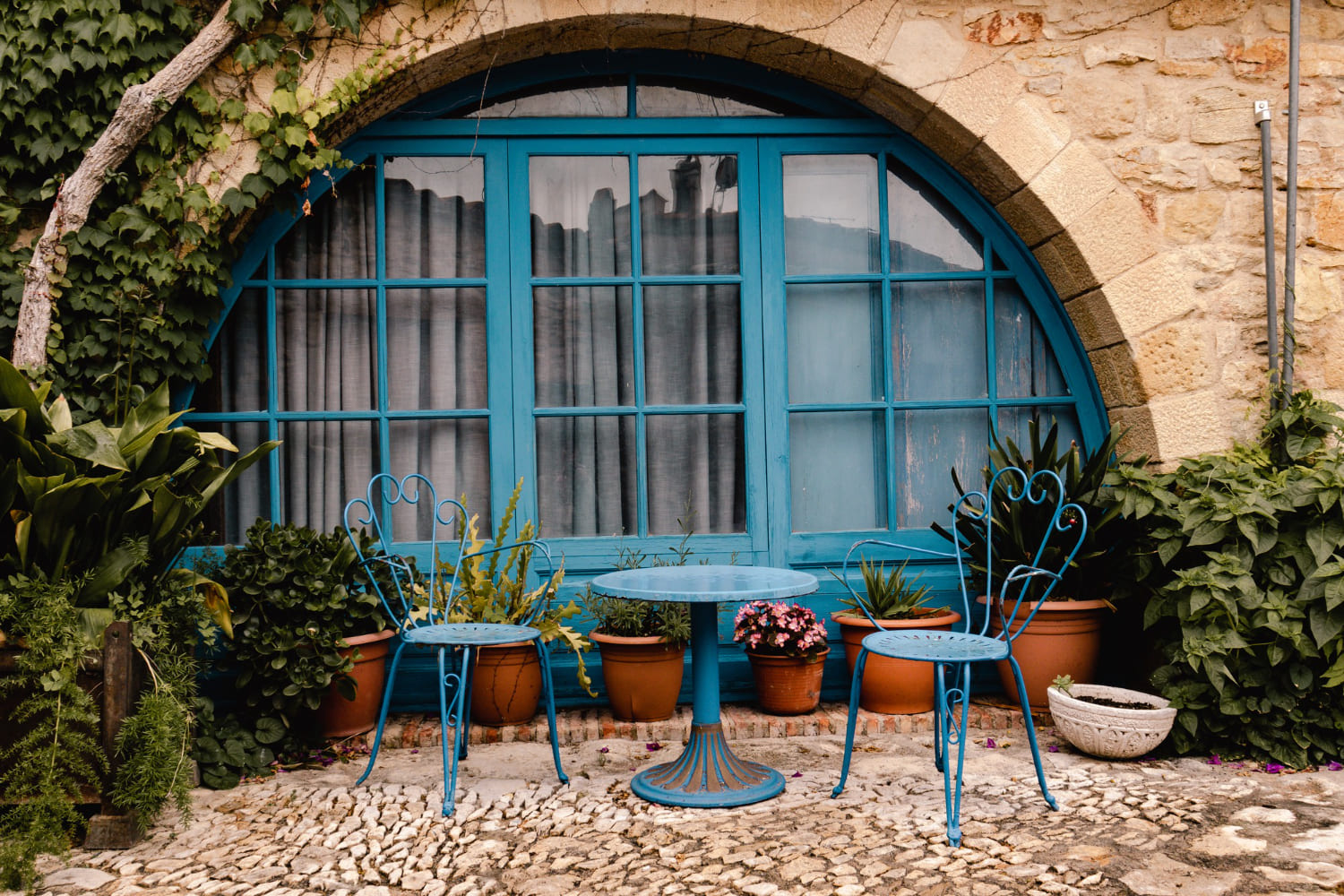 scaune, masa, ferestre albastre cu arcada, plante, mozaic pe jos